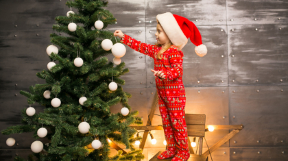 Little girl in pyjamas by the Christmas tree on a wooden chair
